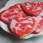 A white porcelain plate holds pink frosted heart shaped sugar cookies