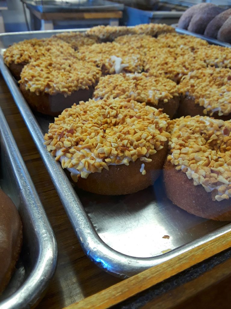 A tray of iced and nut topped doughnuts.