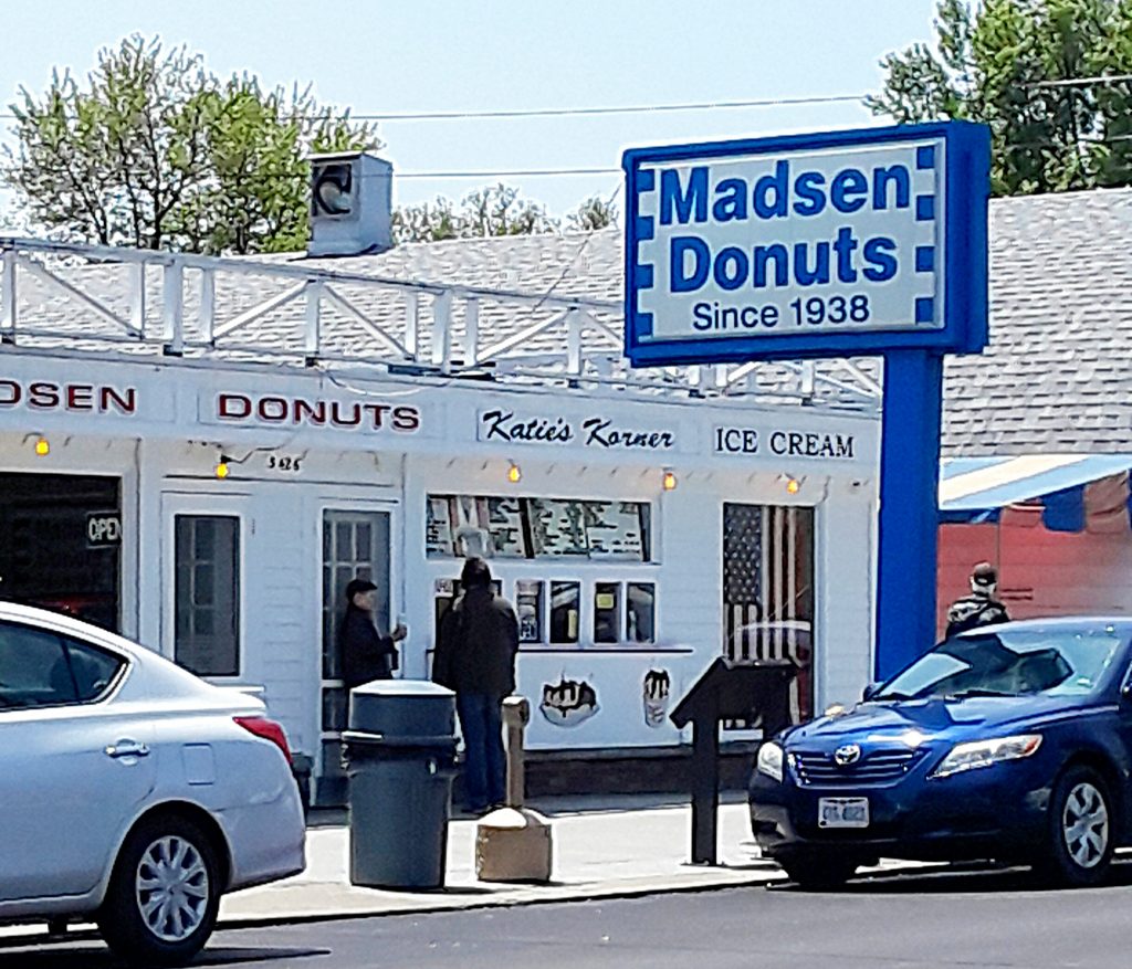 Little white storefront of doughnut shop, with blue and white sign "Madsen Donuts Since 1938."