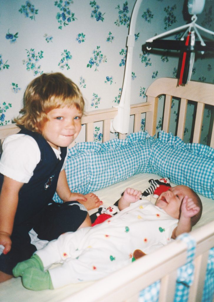 Sister climbs into the crib with her brother.