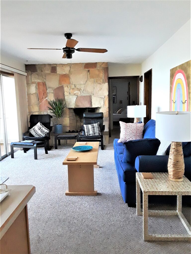 An interior shot of the lake house shows a stone fireplace and blue couch.