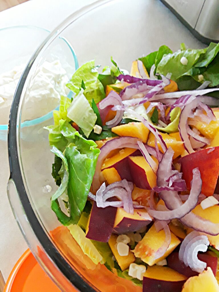 diced peaches, thinly sliced red onion, and greens in a salad bowl