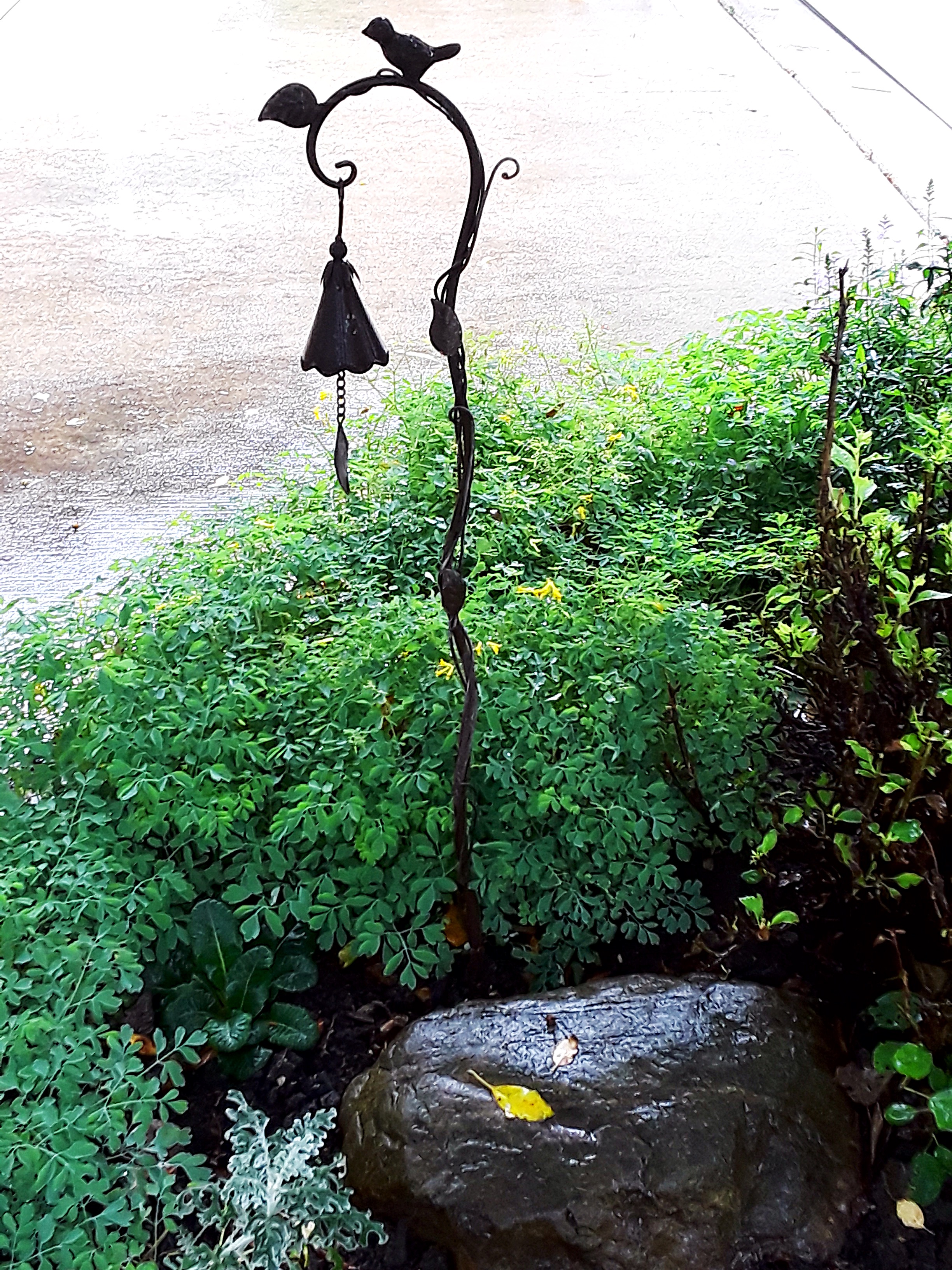 a metalwork bell hangs over a flower border