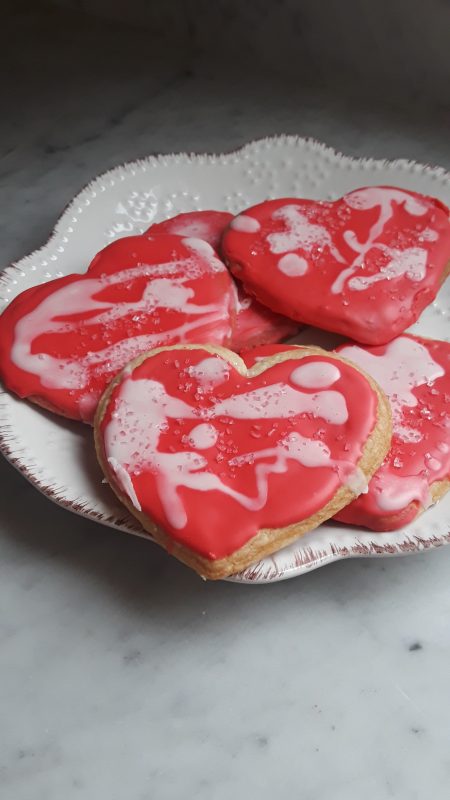 A white porcelain plate holds pink frosted heart shaped sugar cookies