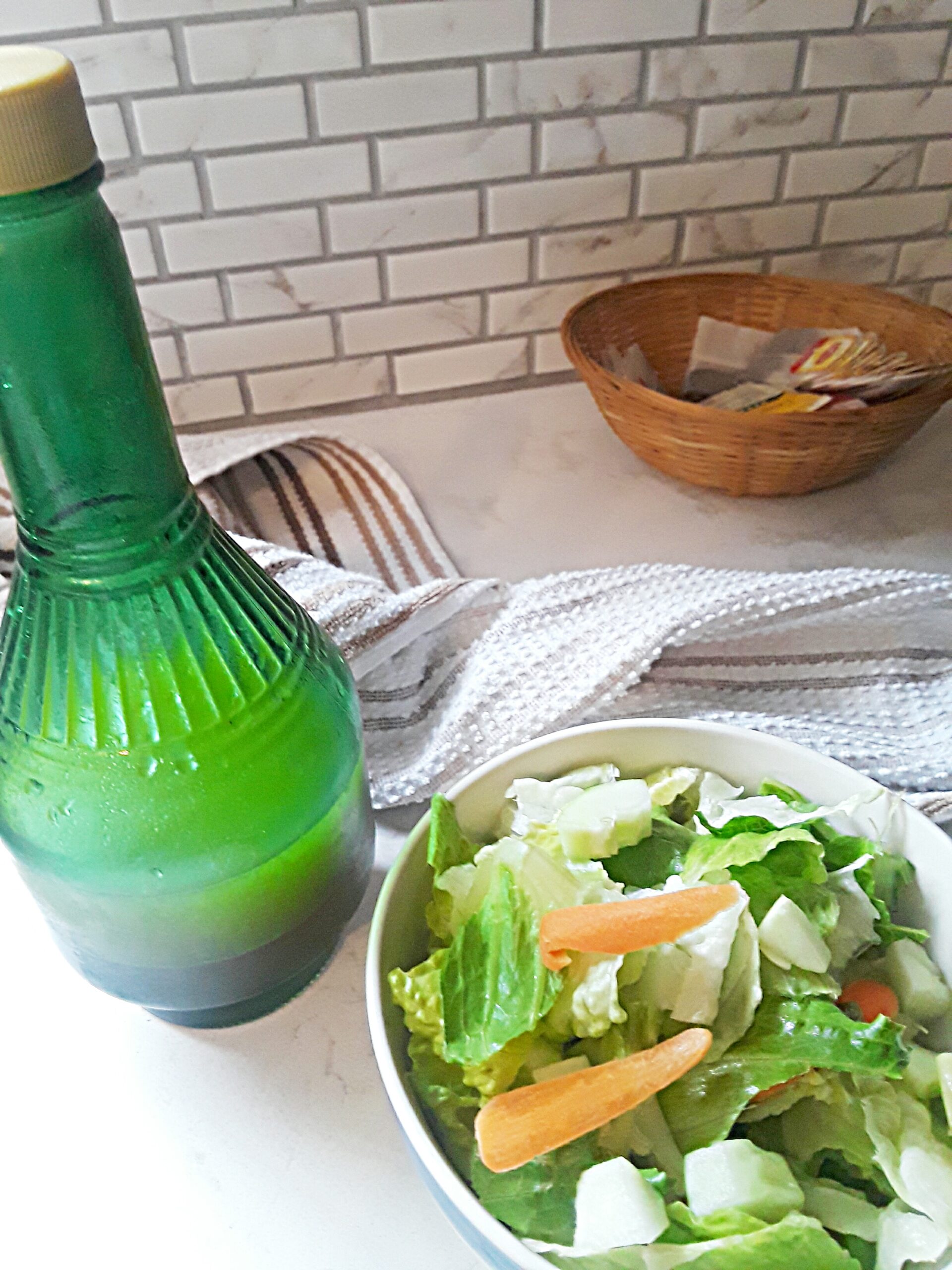 zesty salad dressing in a green bottle next to a crispy green salad.