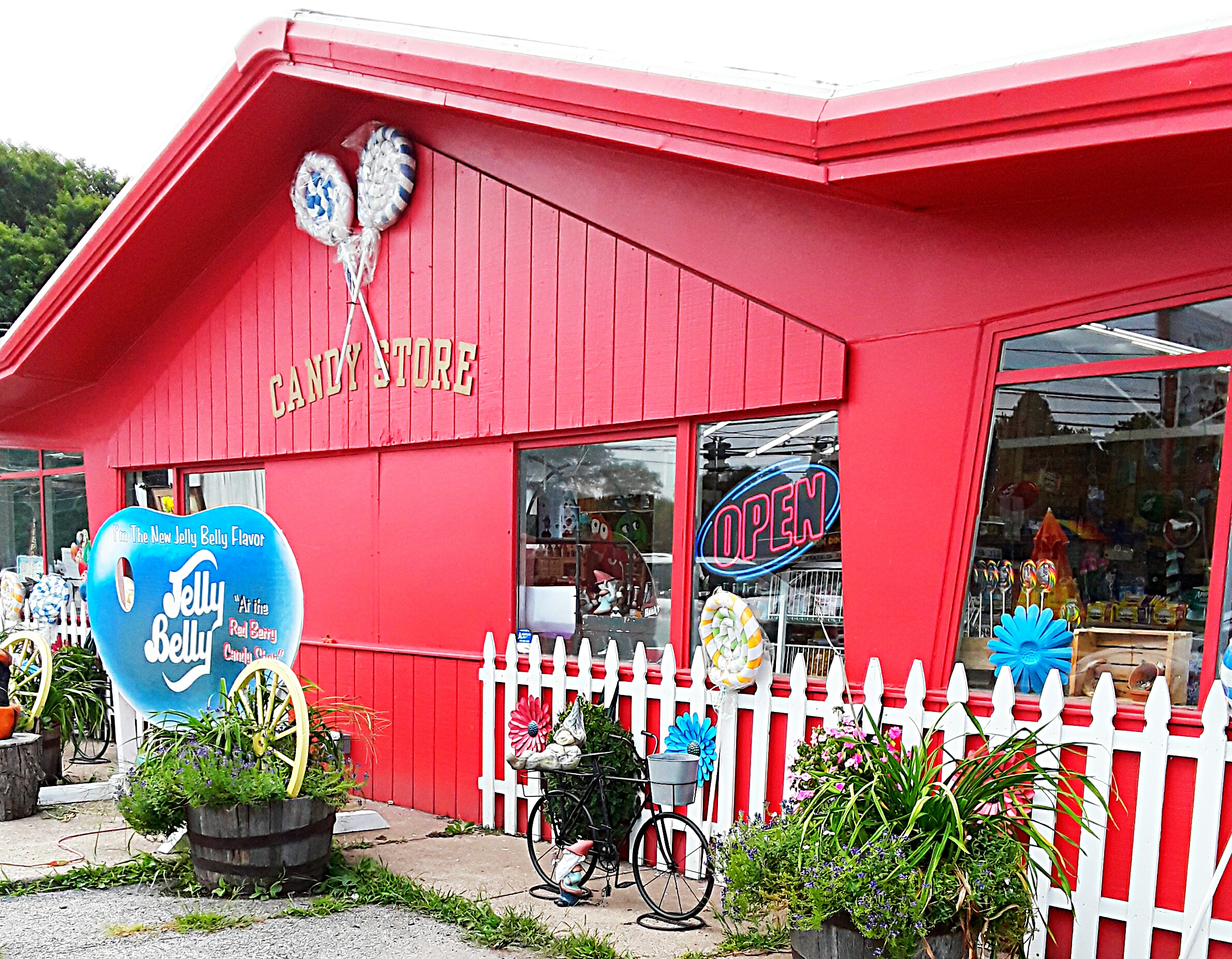 Red clapboard and a white picket fence surround the candy shop